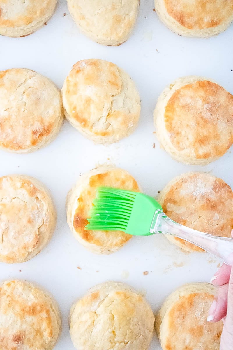 A brush brushing on top of the biscuits the honey and butter mixture.