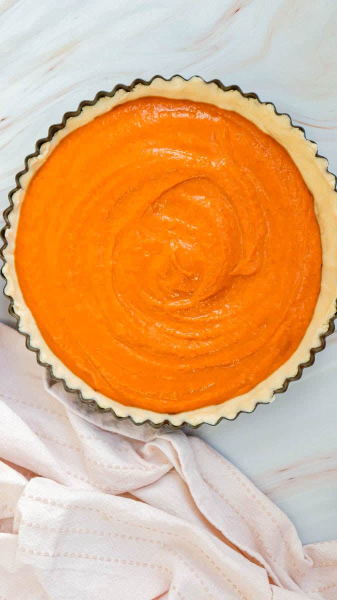 Pumpkin pie filling in pie crust ready to bake.