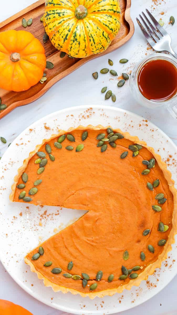 Pumpkin pie on a white plate with pumpkin seeds scattered around it.