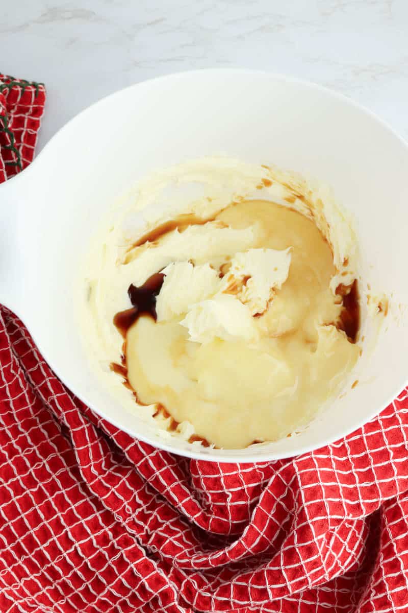Creamed butter with sweetened condensed milk and vanilla extract in white bowl