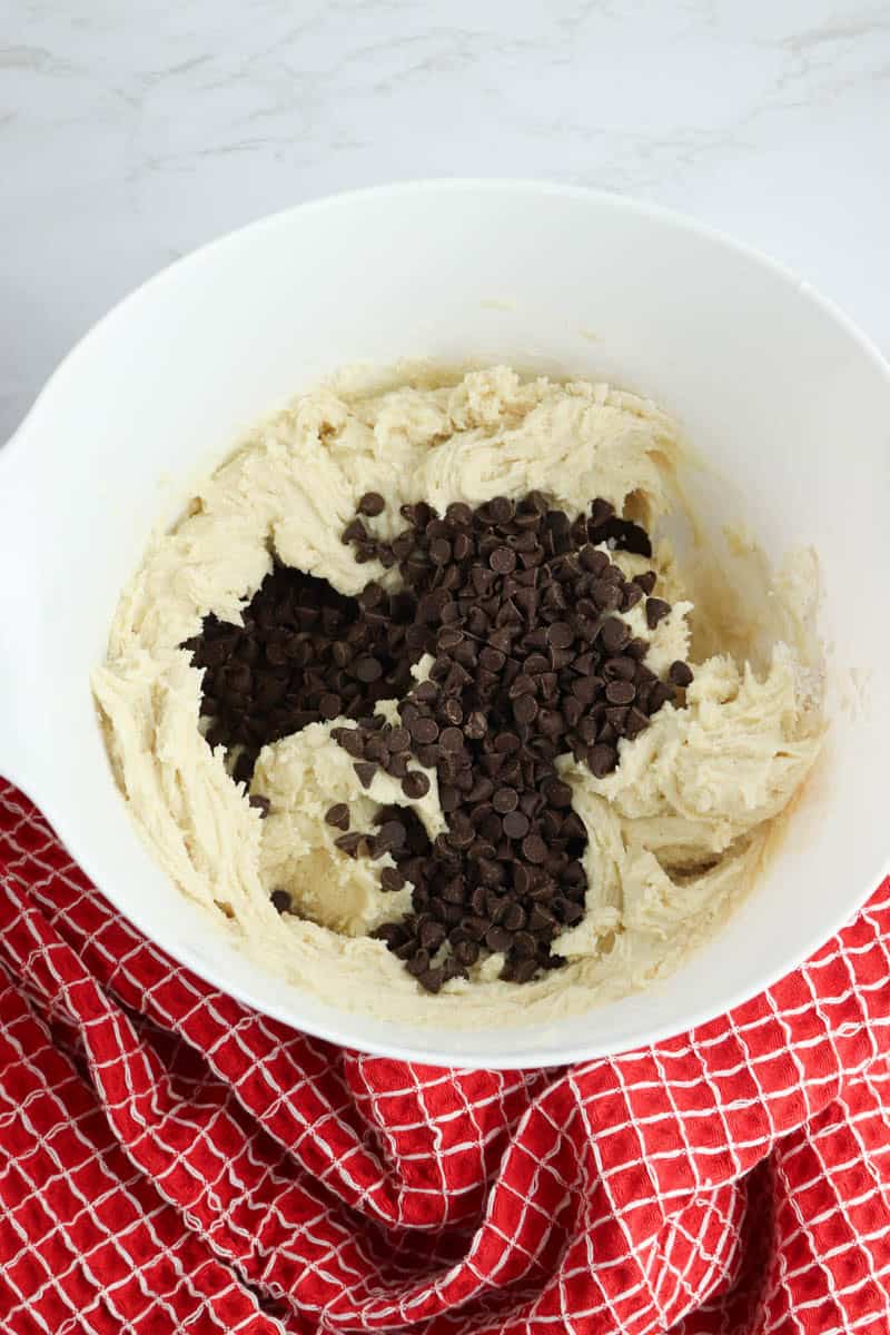 White bowl with butter, sweetened condensed milk, vanilla extract, flour, baking powder and mini chocolate chips.