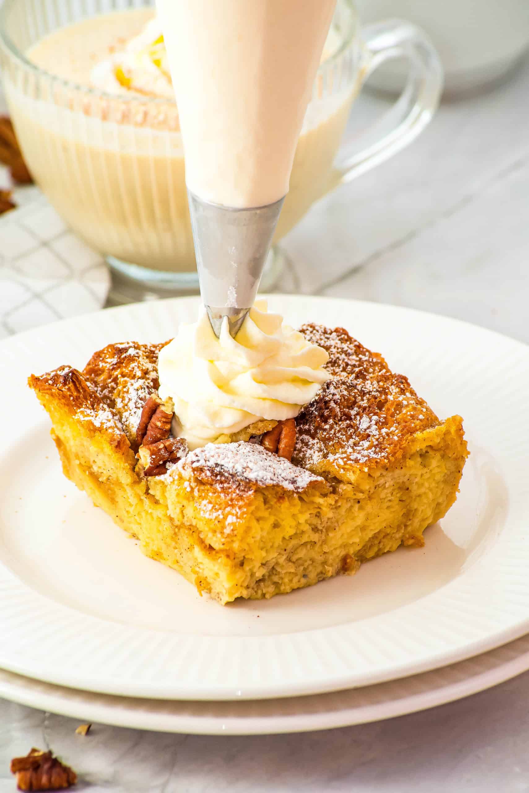 A piece of gluten free eggnog french toast casserole on a white plate with whipped cream on top of the piece.