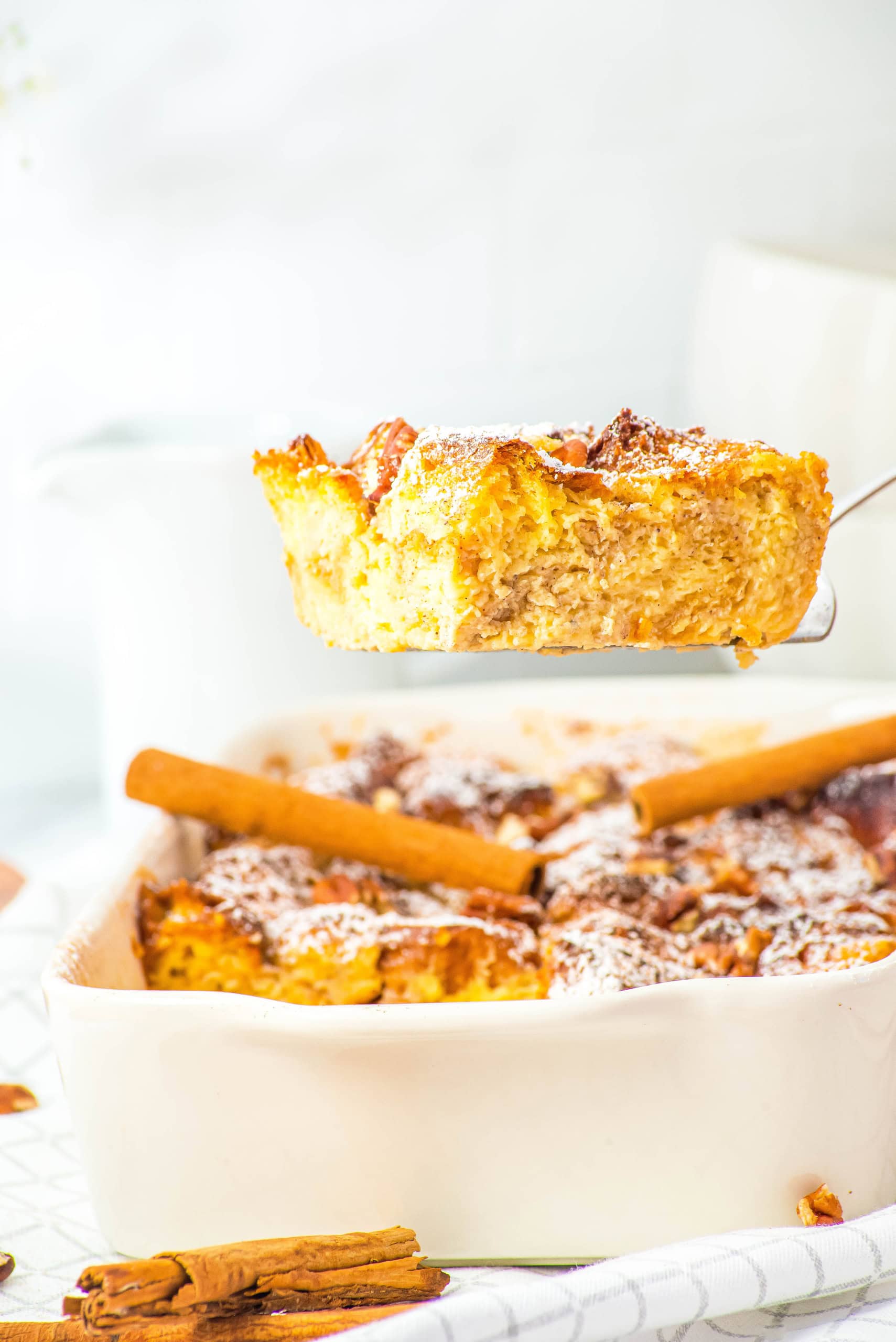A piece of gluten free eggnog french toast being lifted out of the casserole dish.