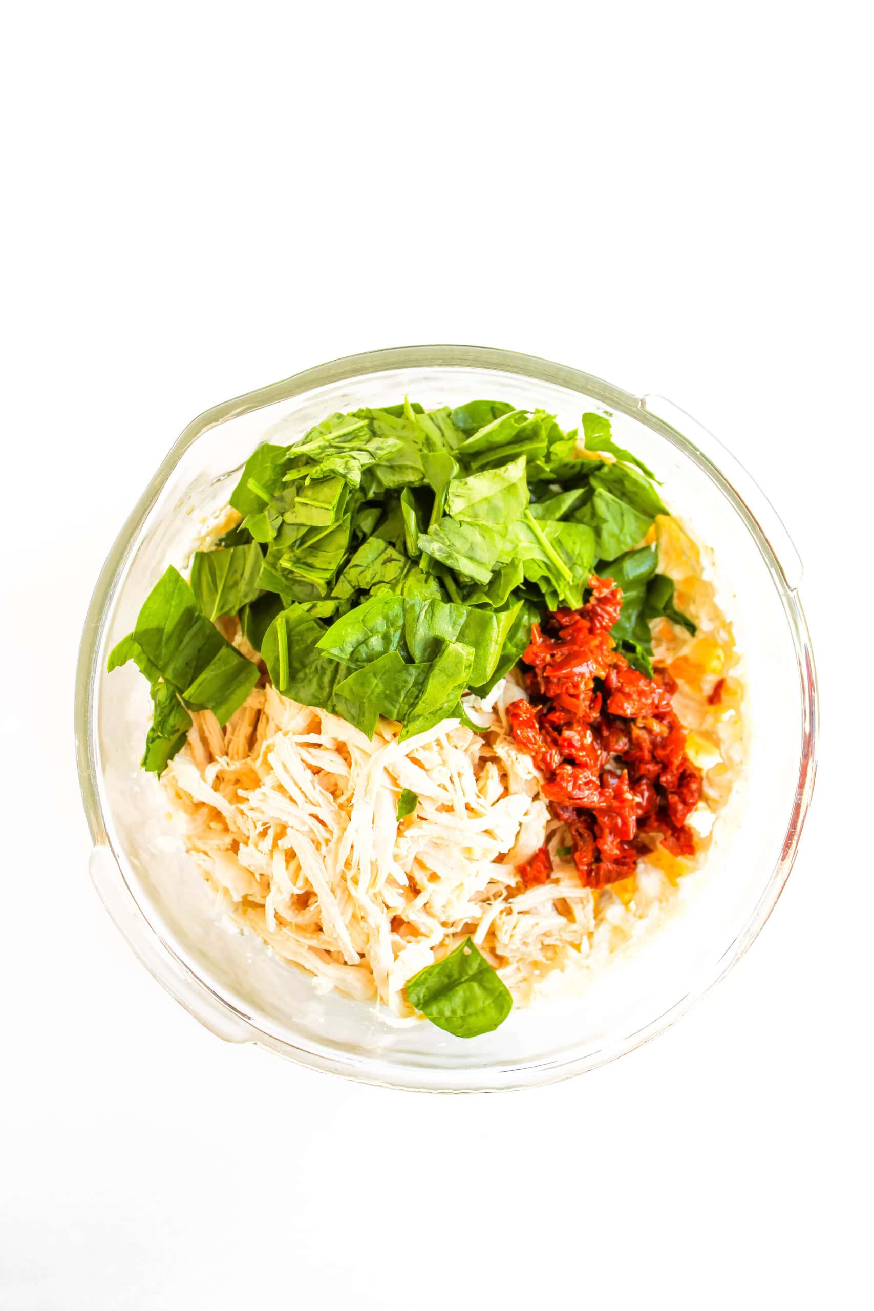 Spinach, sun-dried tomatoes and shredded chicken added to the mix in the bowl.