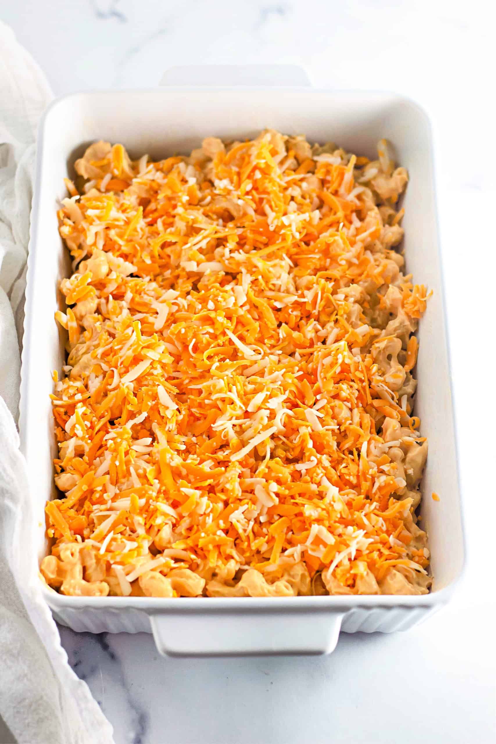 Gluten free mac and cheese in white casserole dish with shredded cheese sprinkled on top.
