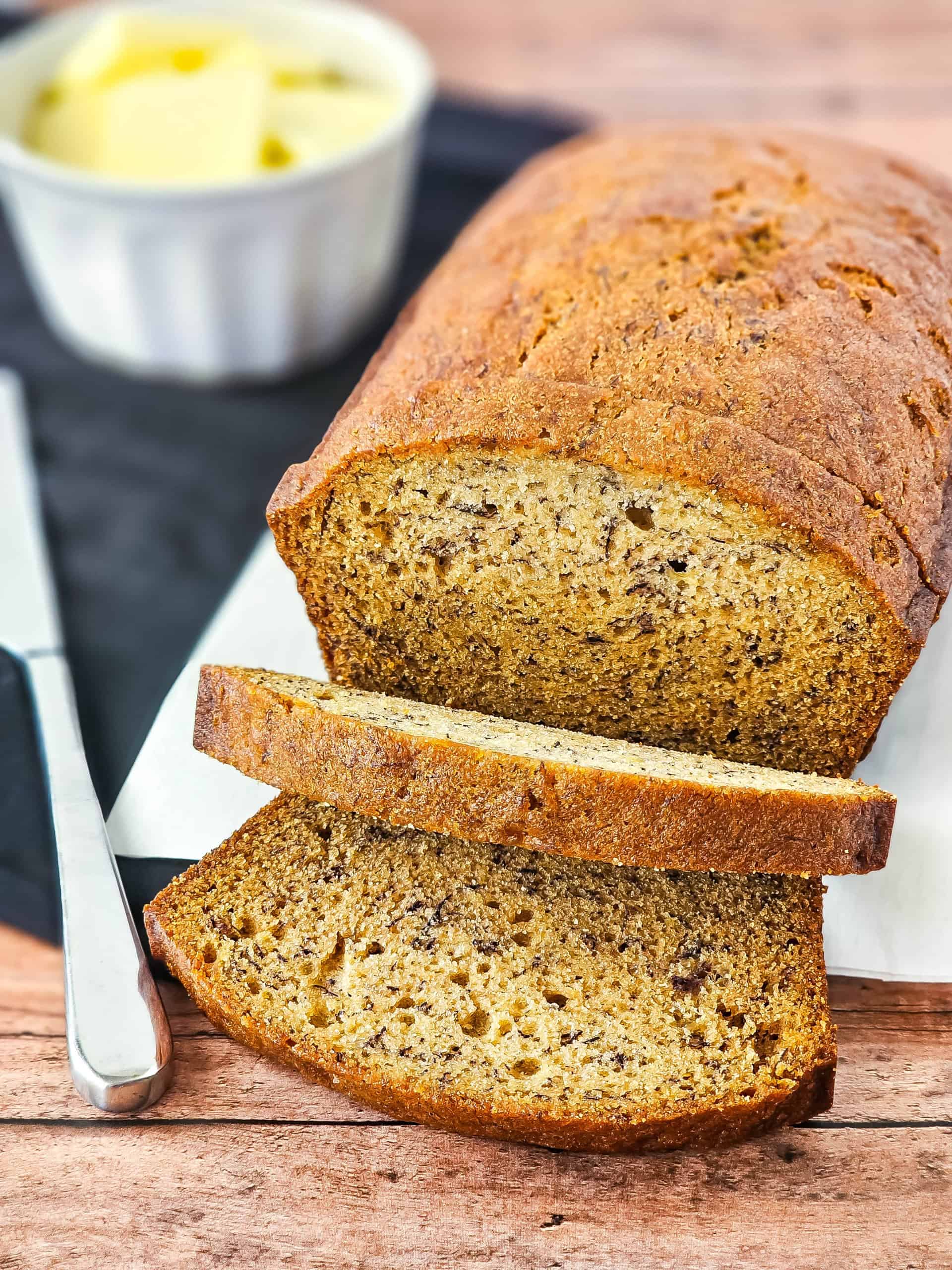 Loaf of gluten free bread on white cutting board with 2 slices cut and knife beside loaf