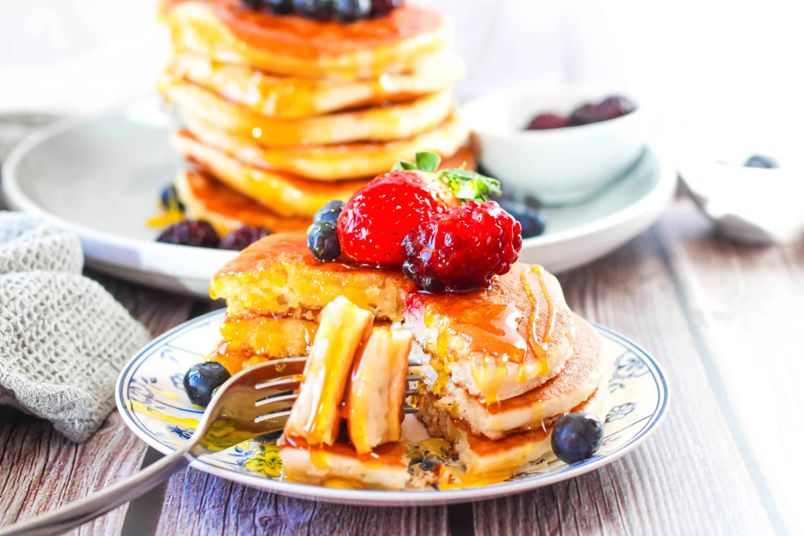 Two plates with stacks of pancakes that are topped with fresh fruit. 