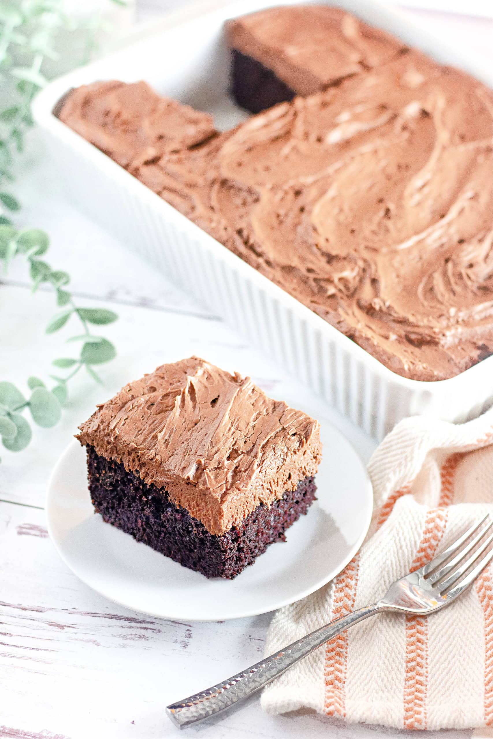 A piece of gluten free chocolate cake on a white plate next to a baking pan with chocolate cake.