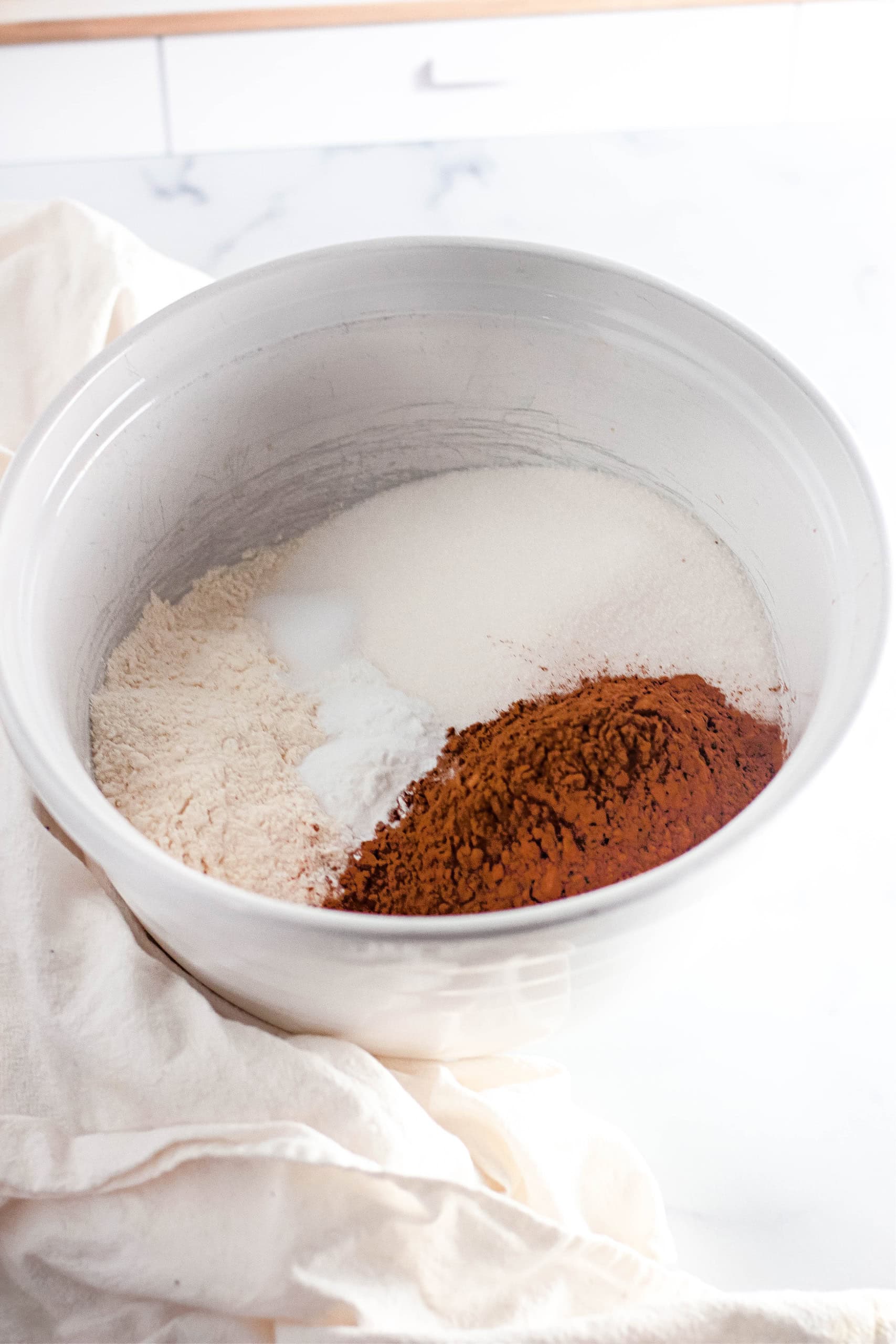 A white bowl with cocoa powder, gluten free flour, sugar, baking powder, baking soda and salt.