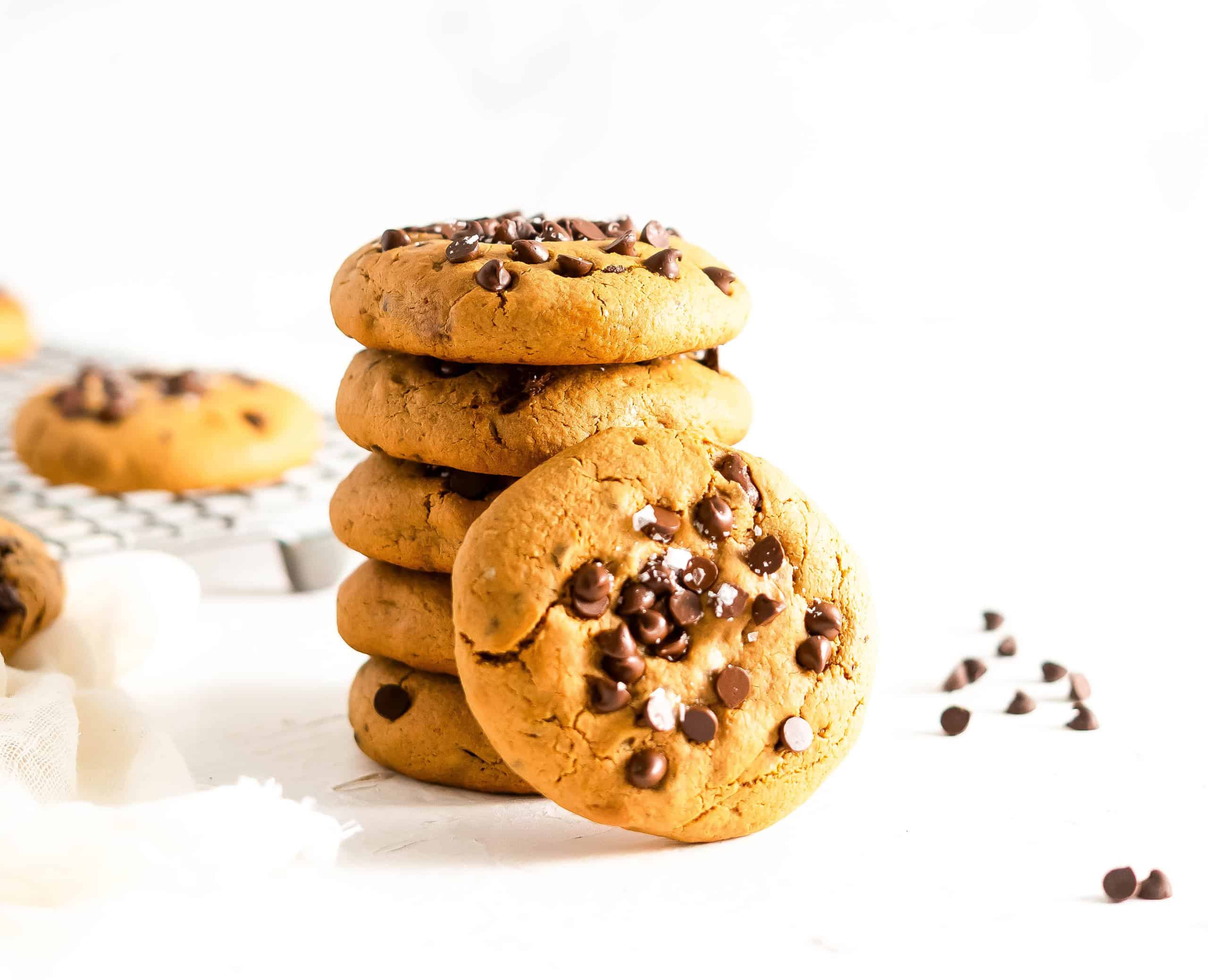A stack of soft baked gluten free chocolate chip cookies with a few chocolate chips on the side.
