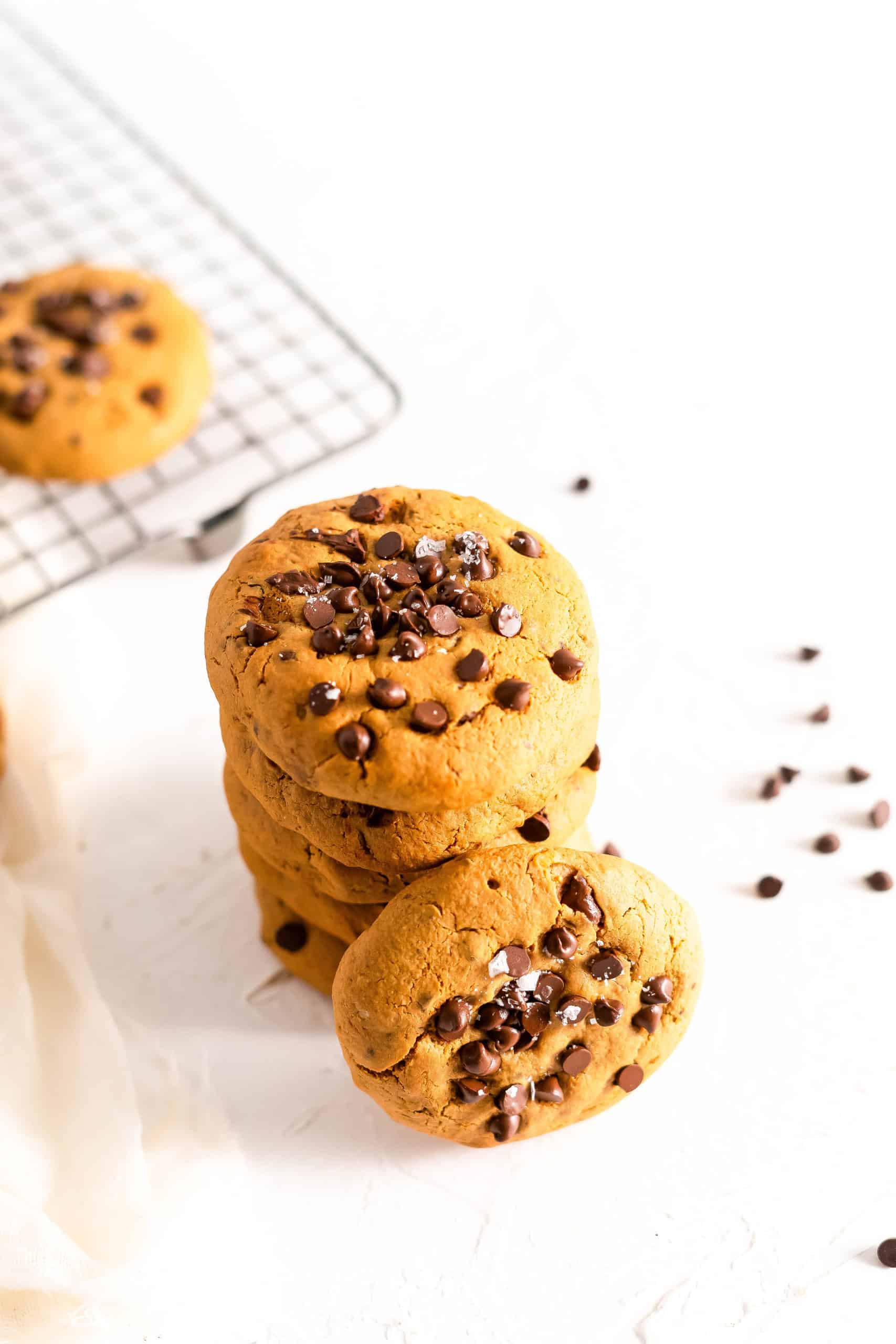 A stack of gluten free soft baked chocolate chip cookies with chocolate chips on the side