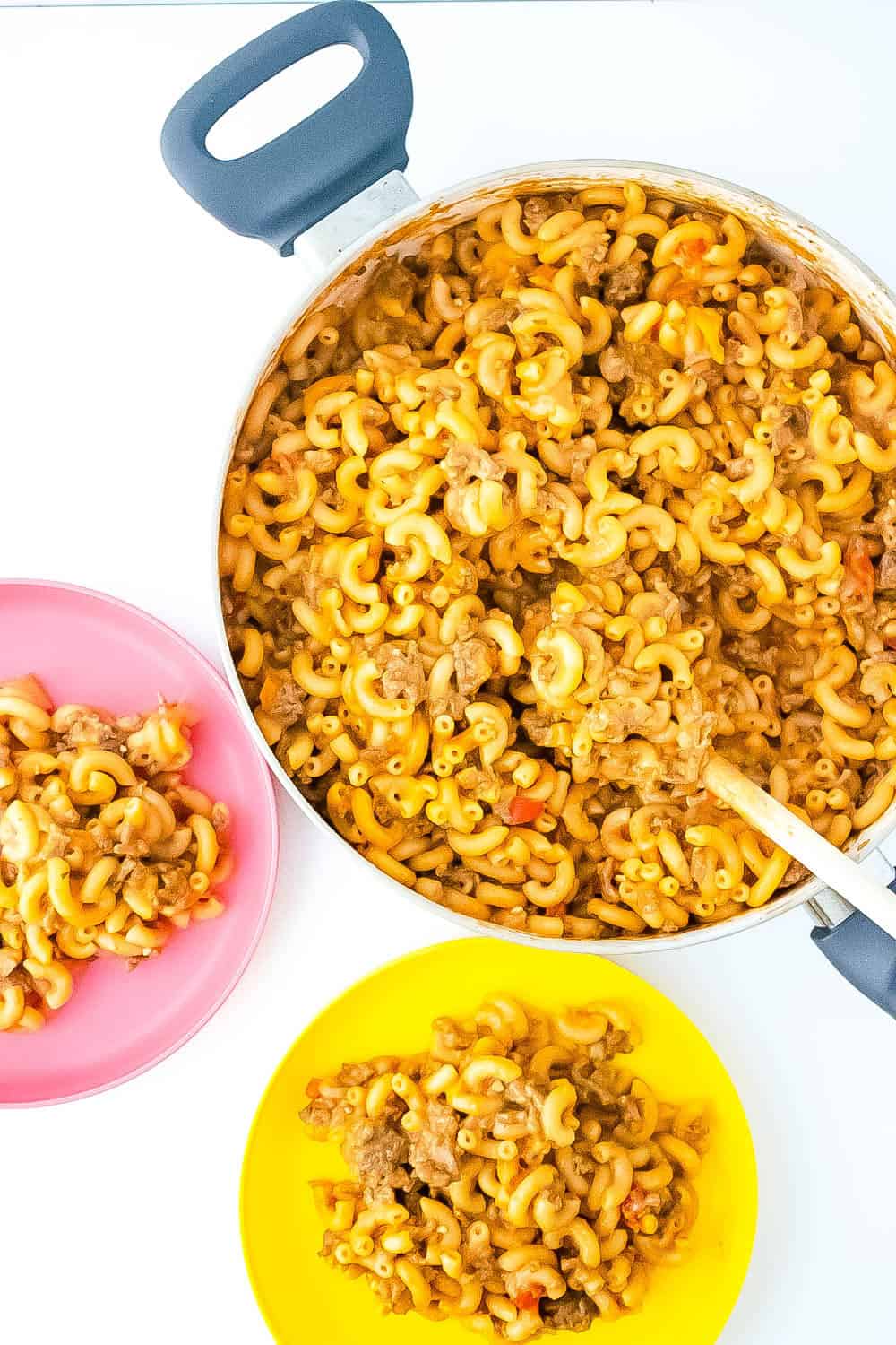 Skillet with gluten free hamburger helper with two plates and a spoon
