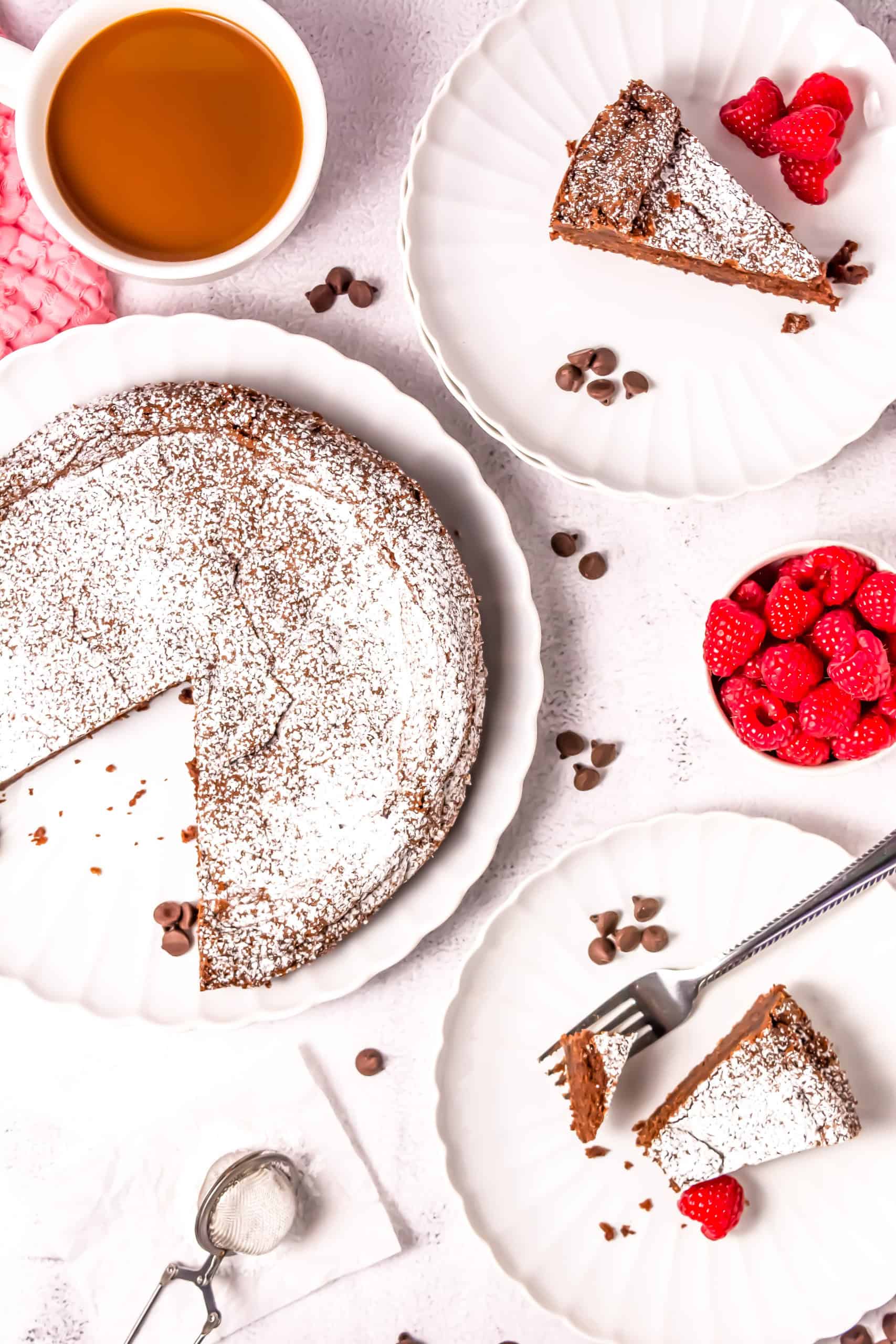 The chocolate torte with slices on white plates with a bowl of raspberries and chocolate chips