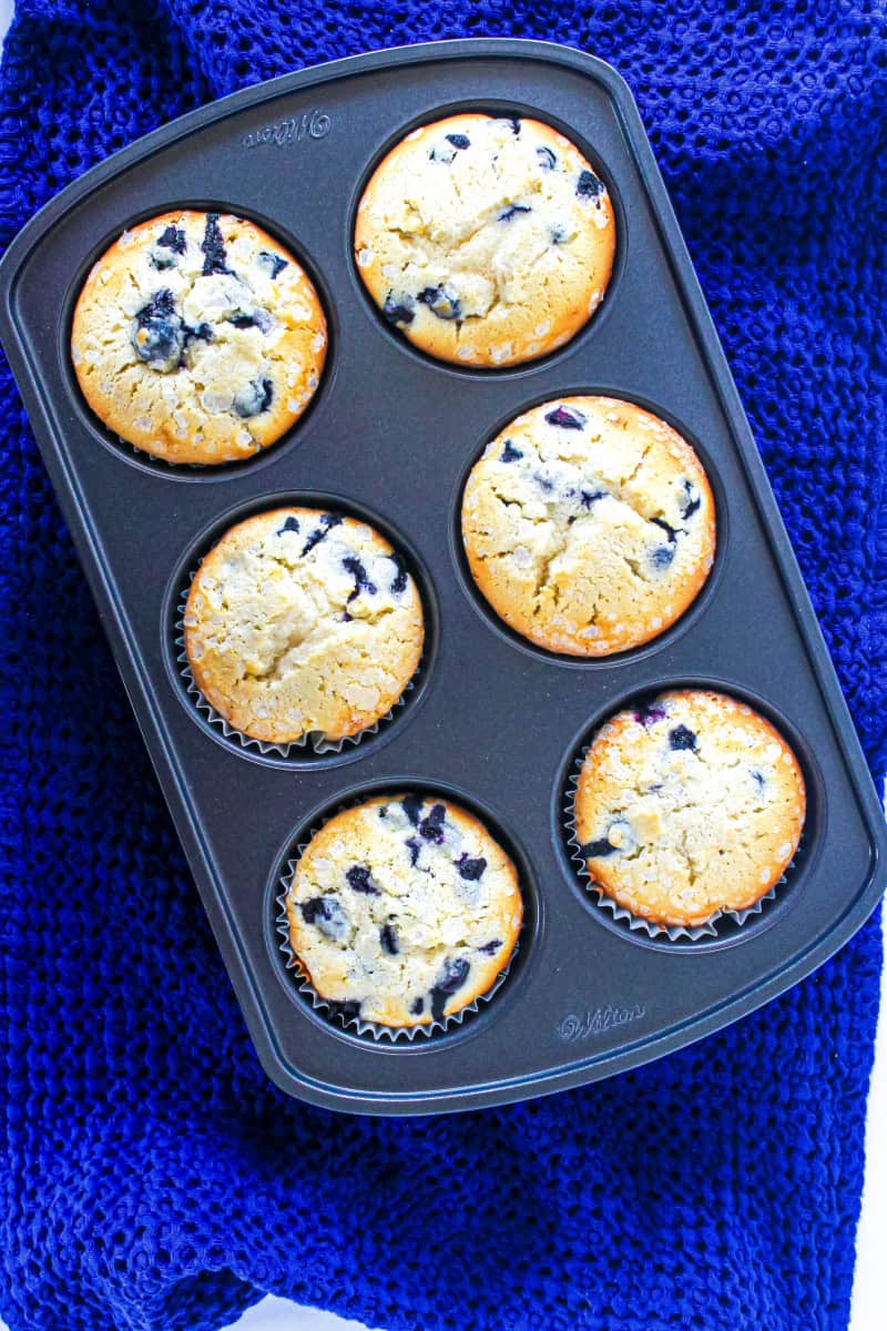 A muffin pan on a blue towel with 6 jumbo gluten free blueberry muffins.