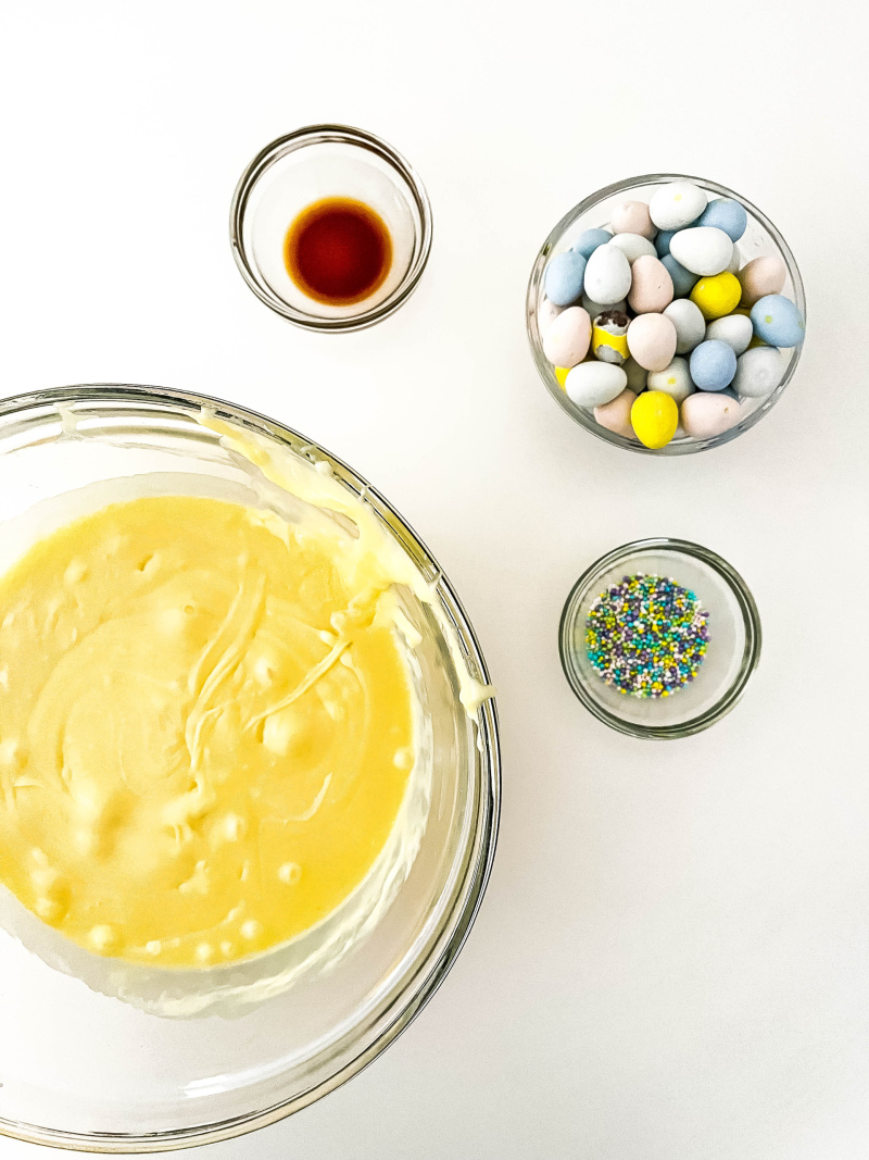 Melted white chocolate, sweetened condensed milk melted together with vanilla extract, sprinkles and mini eggs to go in bowl.