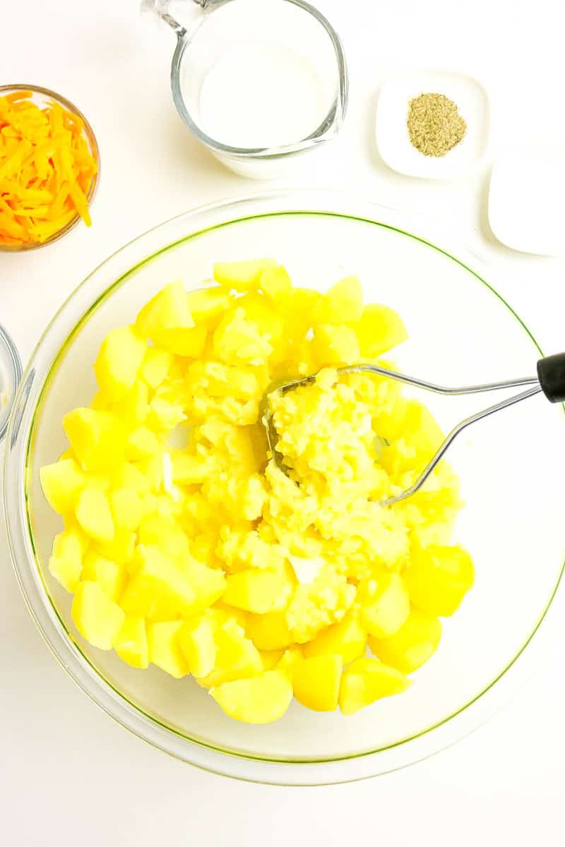 A potato masher mashing the potatoes with butter