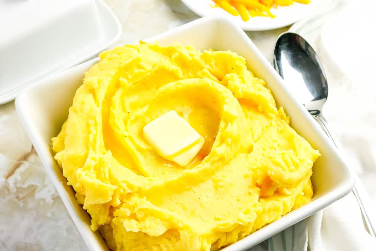 Bowl of cheesy mashed potatoes with butter on top and spoon beside bowl