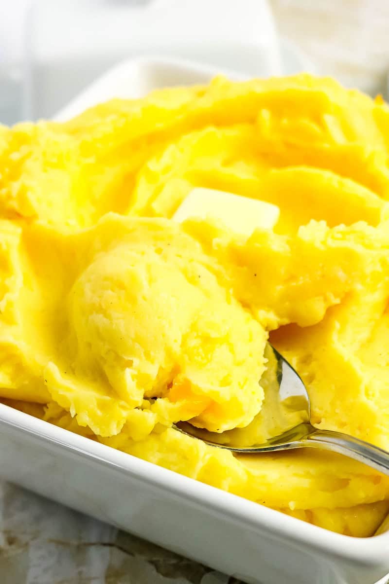 A bowl of the creamy cheesy mashed potatoes with a spoon in it.
