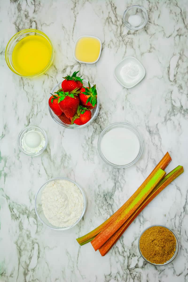 Ingredients for gluten free strawberry rhubarb crumble on a marble background.
