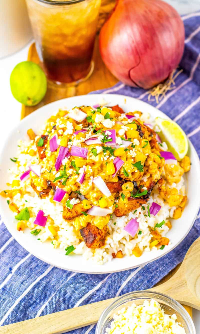 A white bowl with the mexican street corn chicken and rice on a white and blue stripe towel