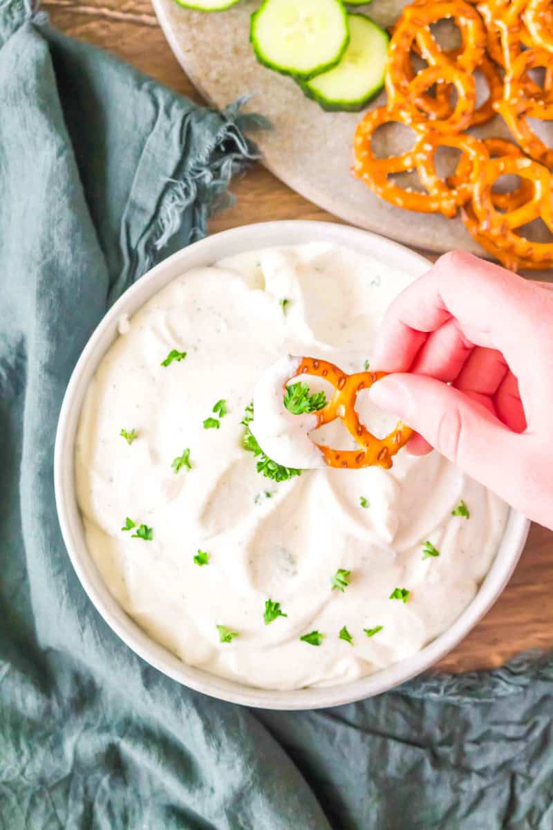 Bowl of cottage cheese ranch dip with hand dipping pretzel