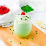 Shamrock shake on wood board with cherries and sprinkles in the background