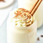 Close up of top of glass of eggnog protein shake that is topped with whipped cream and a cinnamon stick.