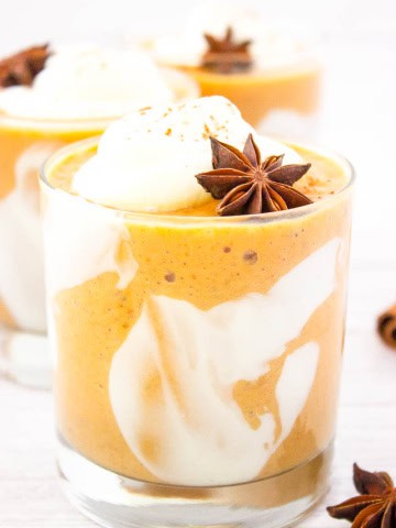 Close up shot a glass with pumpkin pie smoothie in with whipped cream and an allspice star for garnish.
