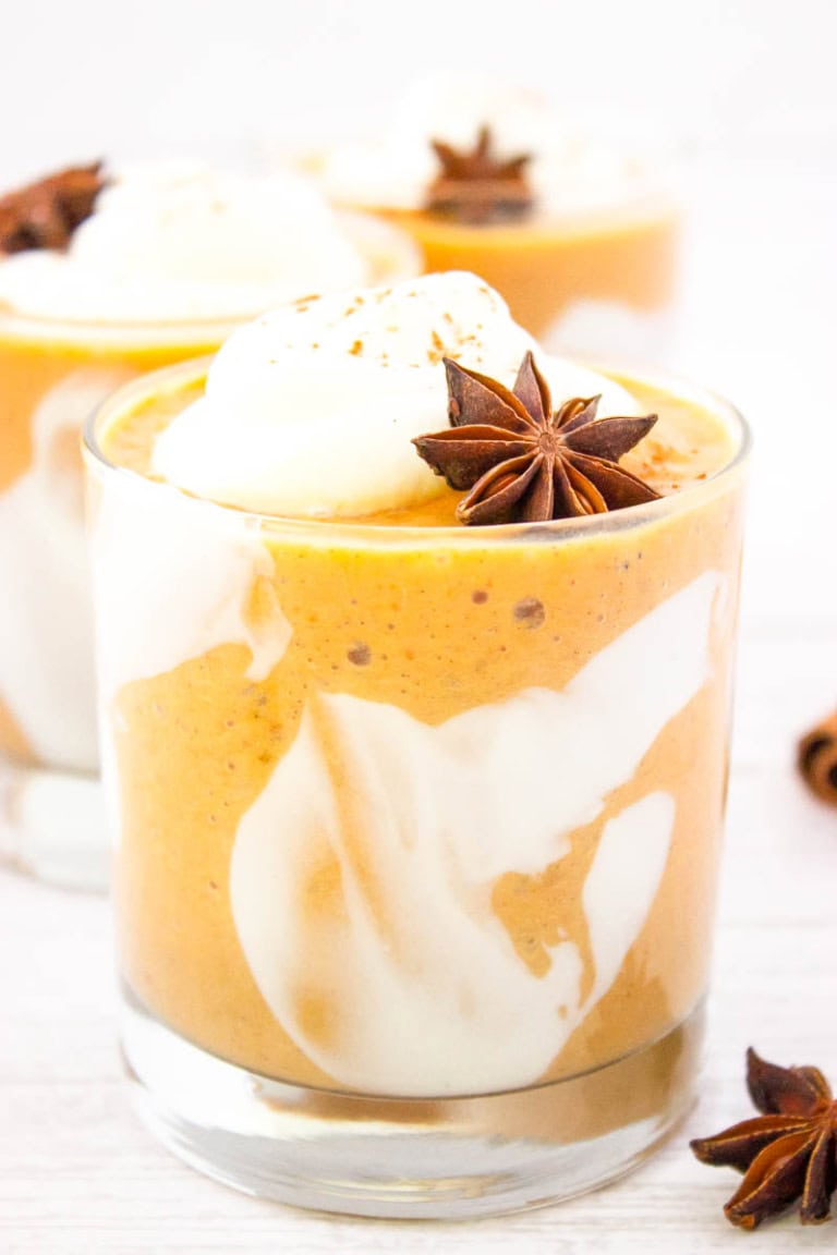 Close up shot a glass with pumpkin pie smoothie in with whipped cream and an allspice star for garnish.