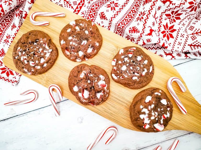 Double chocolate peppermint cookies on wooden board with candy canes surrounding board with a red and white towel in background