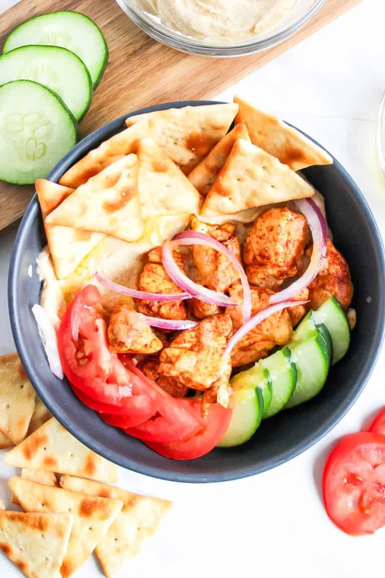Chicken and Hummus Bowl with pita chips, tomatoes, onions, cucumbers topped with dressing.