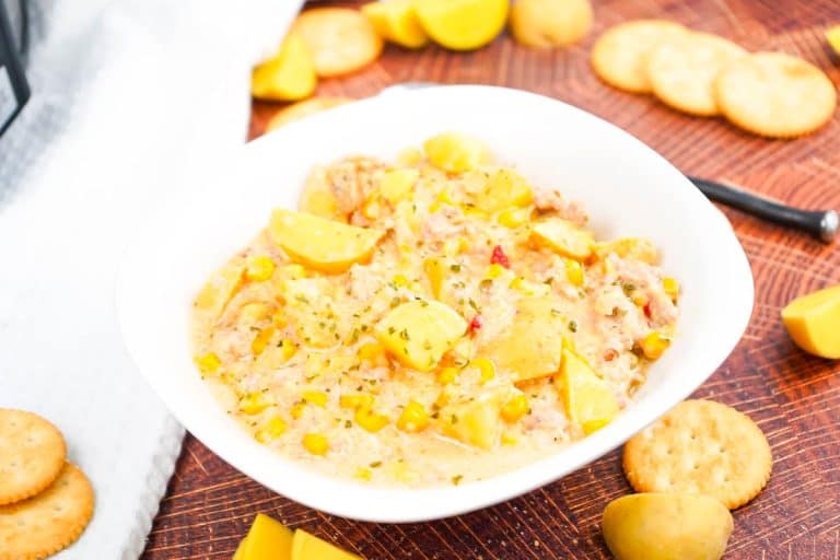 Bowl of sausage and potato soup in bowl on brown backdrop with crackers