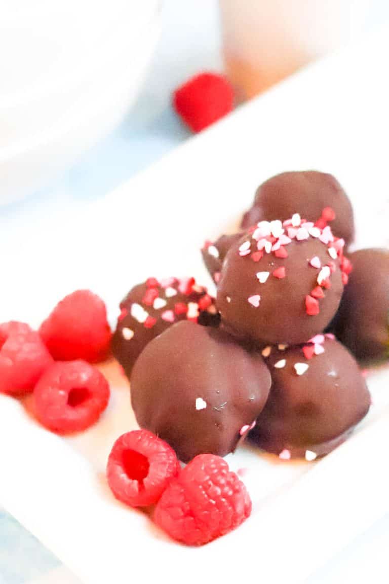 Chocolate Raspberry truffles on white plate stacked with a few raspberries surrounding.