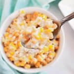 White bowl with mexican street corn with silver spoon on the side and teal towel wrapped around side of bowl.