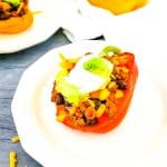 Red bell pepper filled with turkey taco filing on white plate.