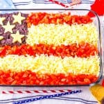 American Flag shaped taco dip in glass baking dish with red, white and blue stripes and stars straws around it.