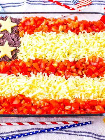 American Flag shaped taco dip in glass baking dish with red, white and blue stripes and stars straws around it.