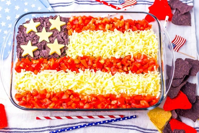 American Flag shaped taco dip in glass baking dish with red, white and blue stripes and stars straws around it.