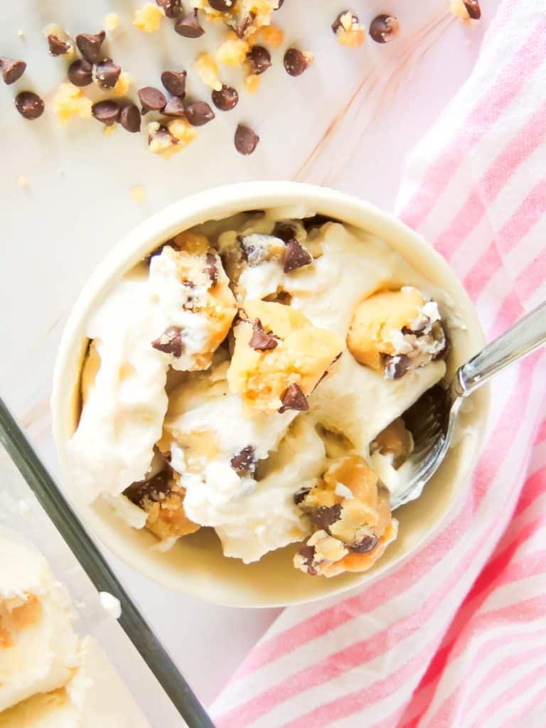 Bowl of cottage cheese cookie dough ice cream with red and white stripe napkin in background on white surface.