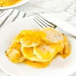 Dairy free cheesy scalloped potatoes on white plate with silver fork on plate with a black and white stripe napkin tucked under plate.