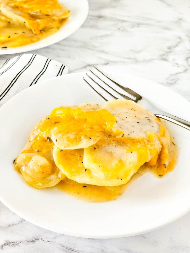 Dairy free cheesy scalloped potatoes on white plate with silver fork on plate with a black and white stripe napkin tucked under plate.