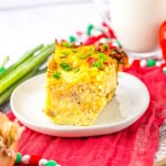 Slice of breakfast casserole on white plate that is on red napkin with glass of milk in the background.