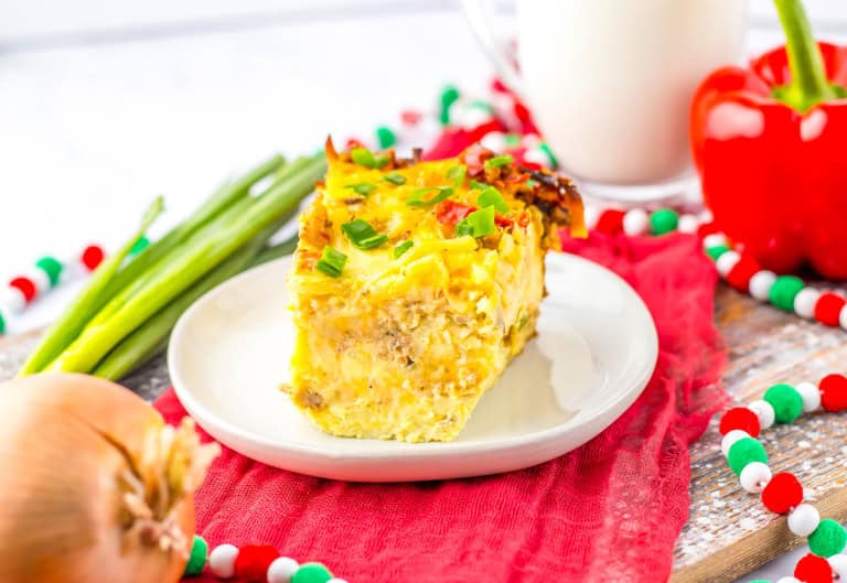 Slice of breakfast casserole on white plate that is on red napkin with glass of milk in the background.