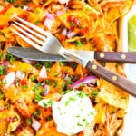 Bottom right corner of sheet pan bbq chicken nachos with fork and knife over the chips.