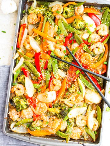 Shrimp and vegetables on one sheet pan with black chopsticks across it. Blue napkin underneath pan on white background.