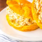 Close up of marry me chicken salad on croissant roll on white plate.