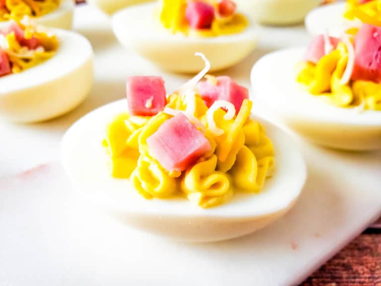 Close up of one ham and cheese deviled egg on white cutting board