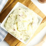 White bowl with mashed potatoes on wooden cutting board