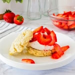 White plate with strawberry shortcake and strawberries in a bowl in the background