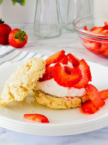 White plate with strawberry shortcake and strawberries in a bowl in the background